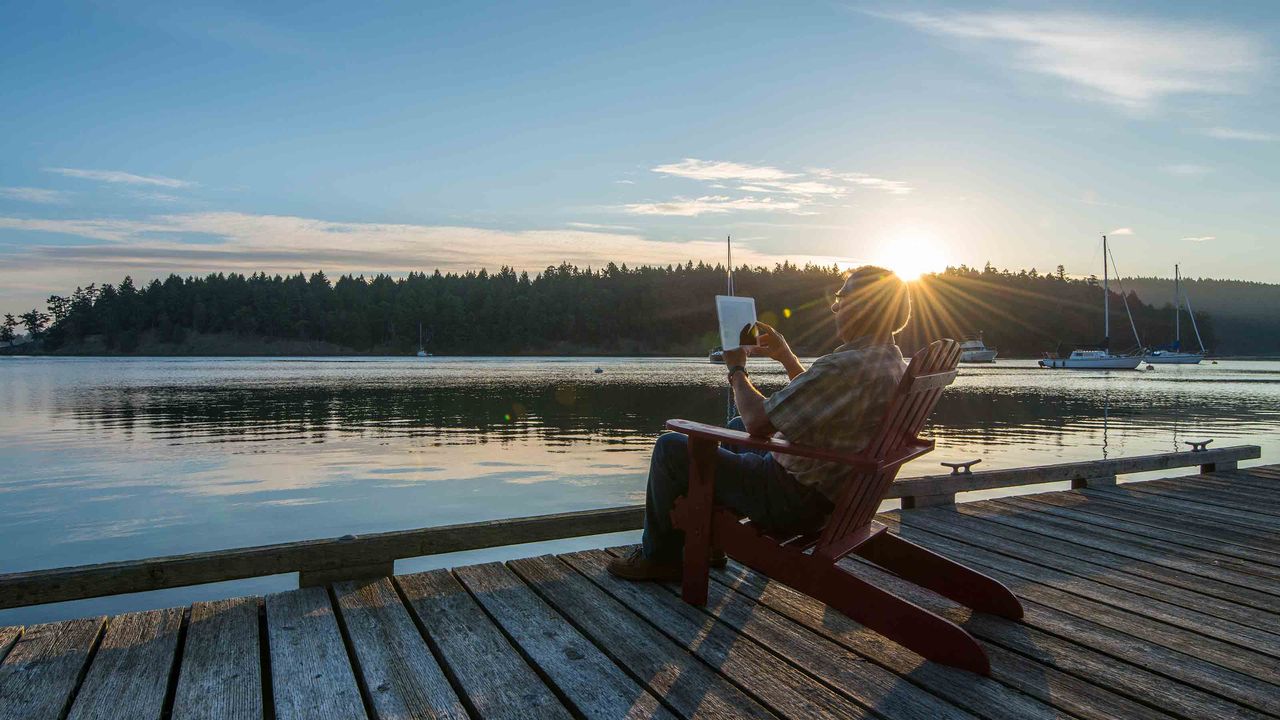 Senior man uses digital tablet on wooden pier, sun