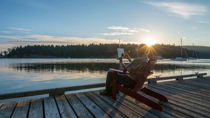 Senior man uses digital tablet on wooden pier, sun