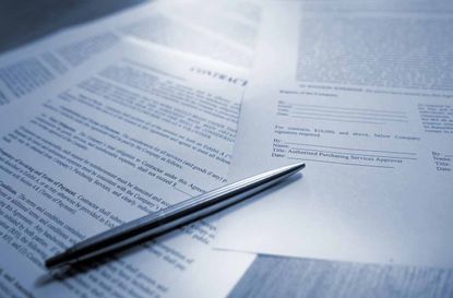 A blue tinted image of silver ball point pen lying on scattered legal contract documents on a wooden table, ready to sign to complete the deal. This conceptual image is shot with a shallow de