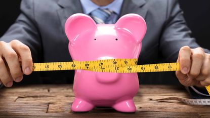 man with measuring tape around piggy bank