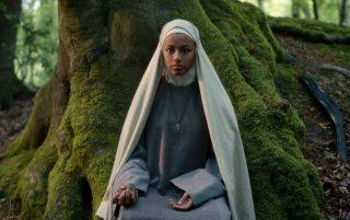 Shalom Brune-Franklin in character as Sister Igraine, sitting in a forest